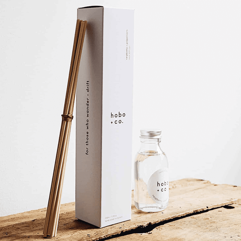 Hobo+Co. Himbeer-Pfeffer-Diffusor mit Stäbchen und Flasche auf einem Holztisch.